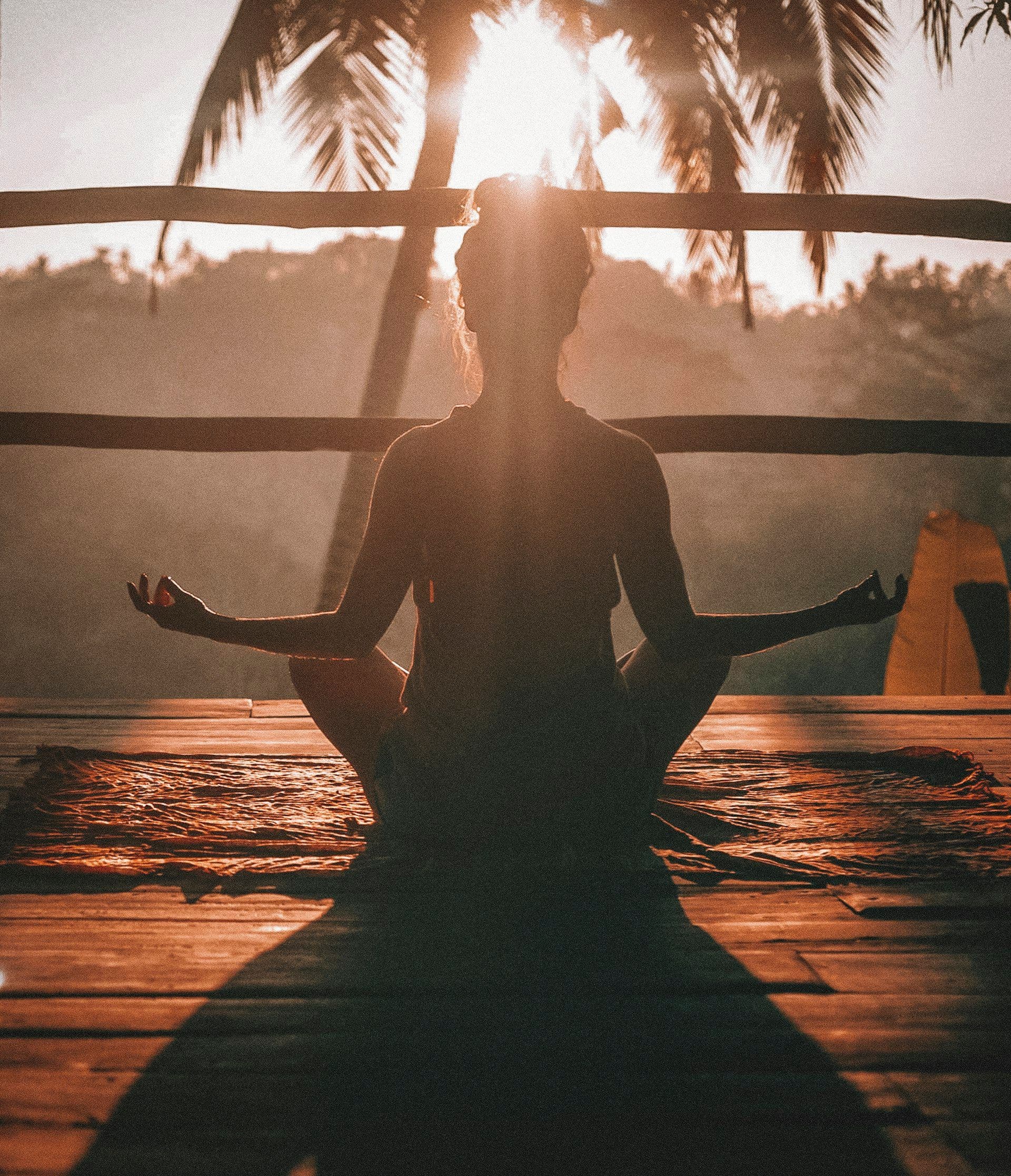 Woman meditating on a wooden deck at sunset