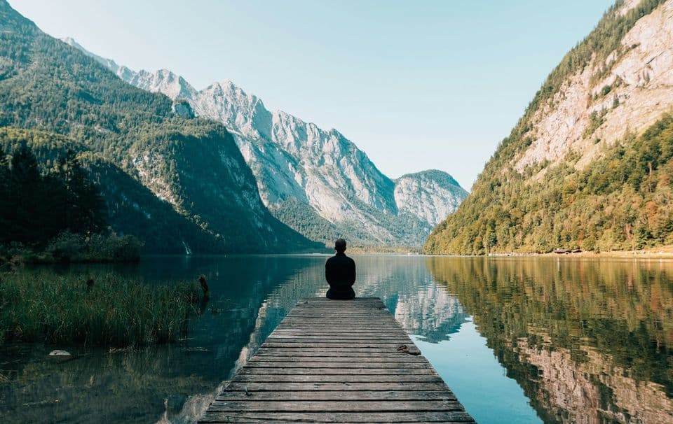 Meditating at the end of a pier on a calm mountain lake