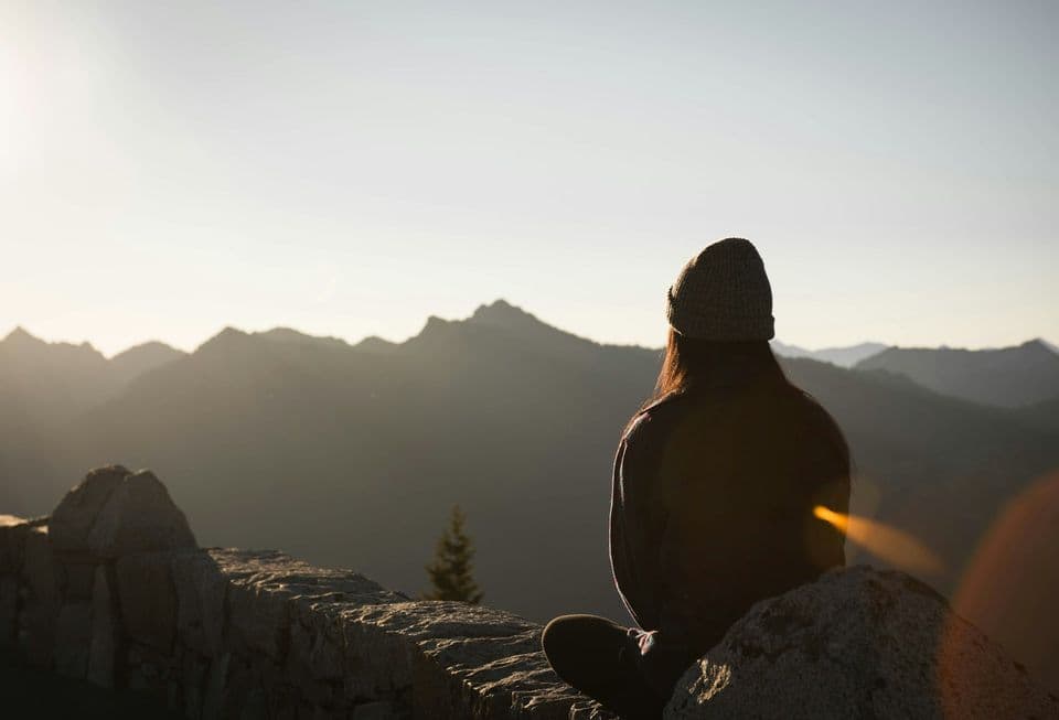 Person sitting peacefully facing mountains at sunrise