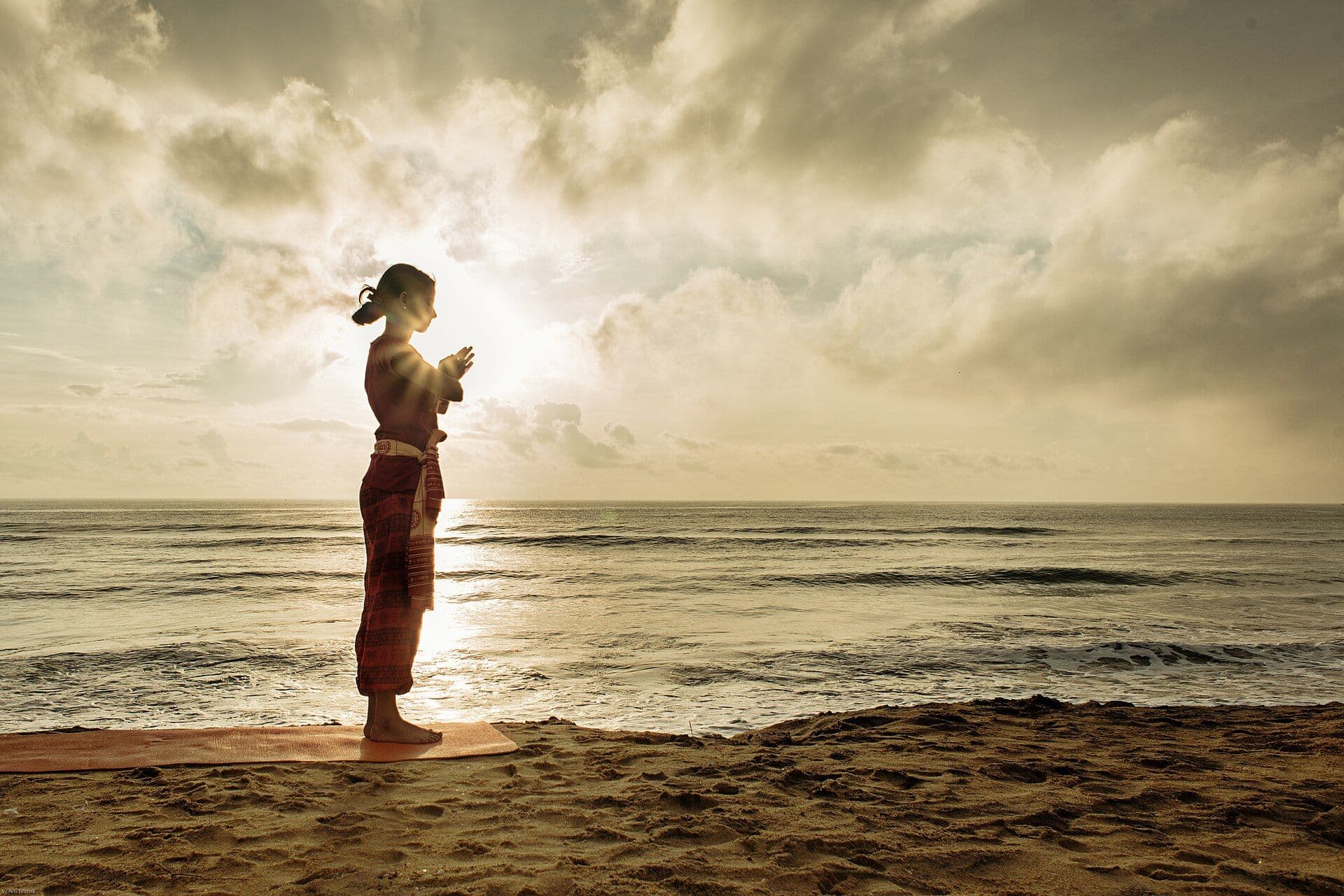 Yoga practitioner in namaste at sunrise on the beach